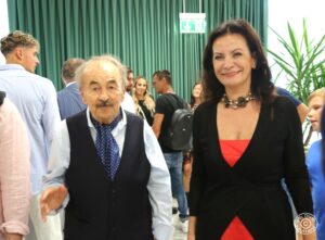 Un momento di dialogo e sorrisi durante un evento conviviale: una donna con un vestito rosso e un uomo anziano che sorridono