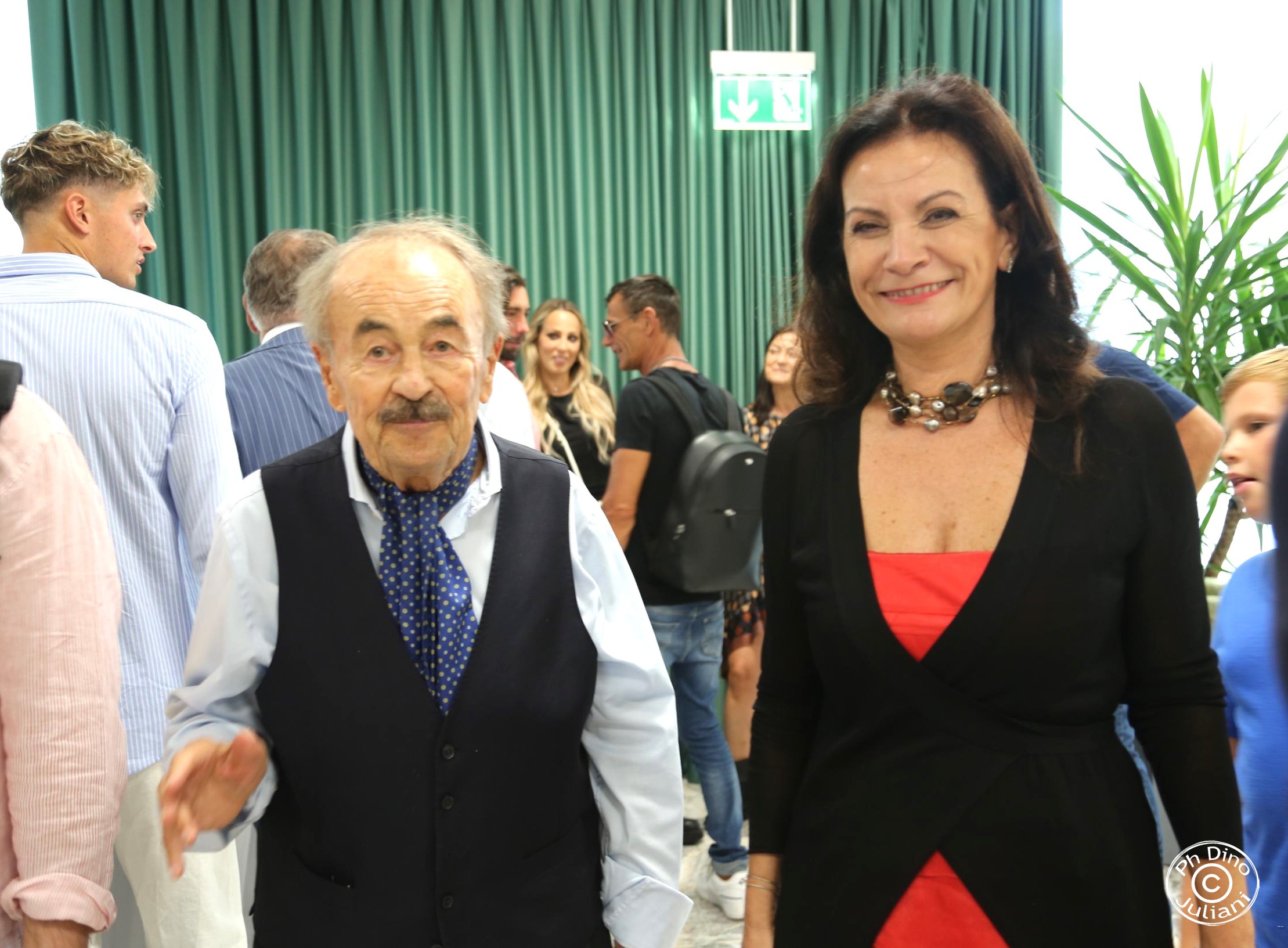 Un momento di dialogo e sorrisi durante un evento conviviale: una donna con un vestito rosso e un uomo anziano che sorridono
