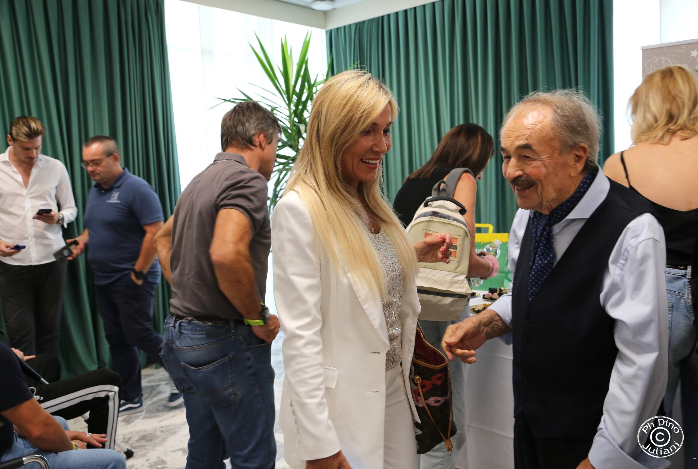 Persone sorridenti che chiacchierano a un evento informale al chiuso, davanti a un tavolo con cibo.