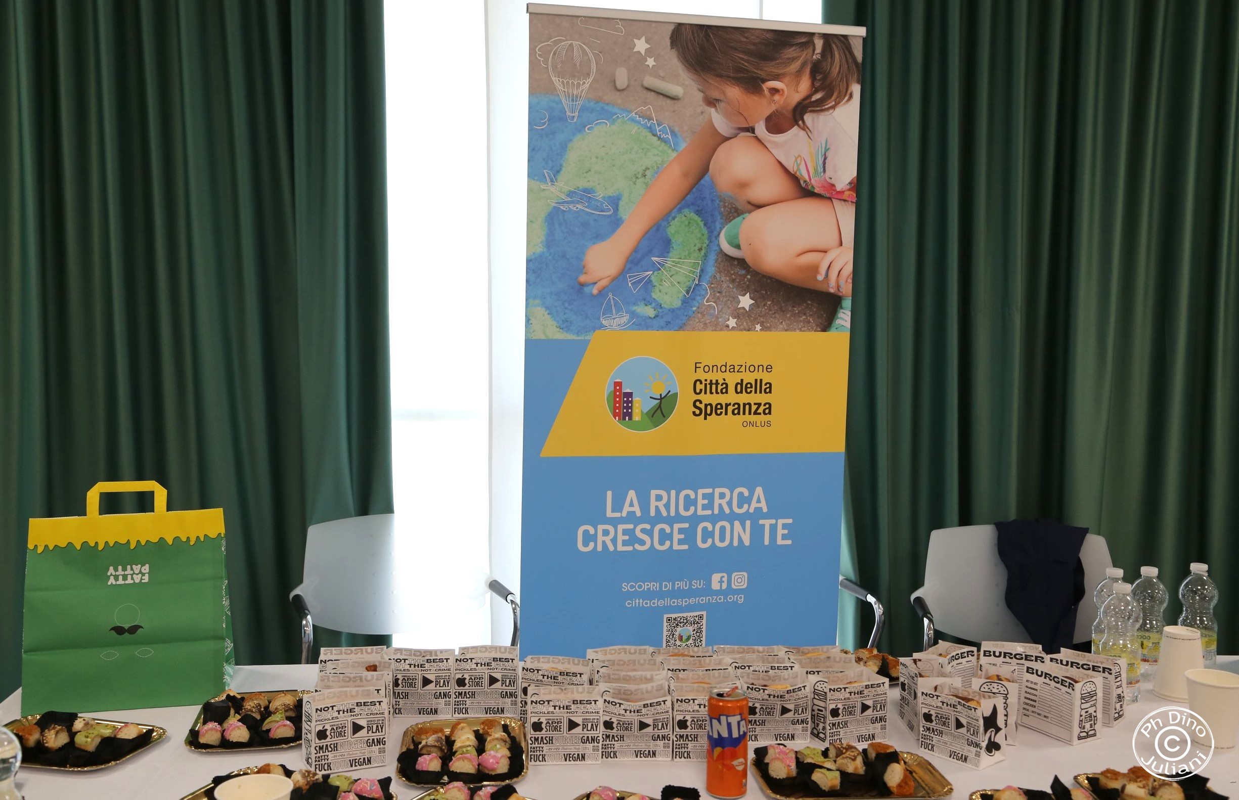 Tavolo con cibo vegano davanti a un roll-up della Fondazione Città della Speranza.