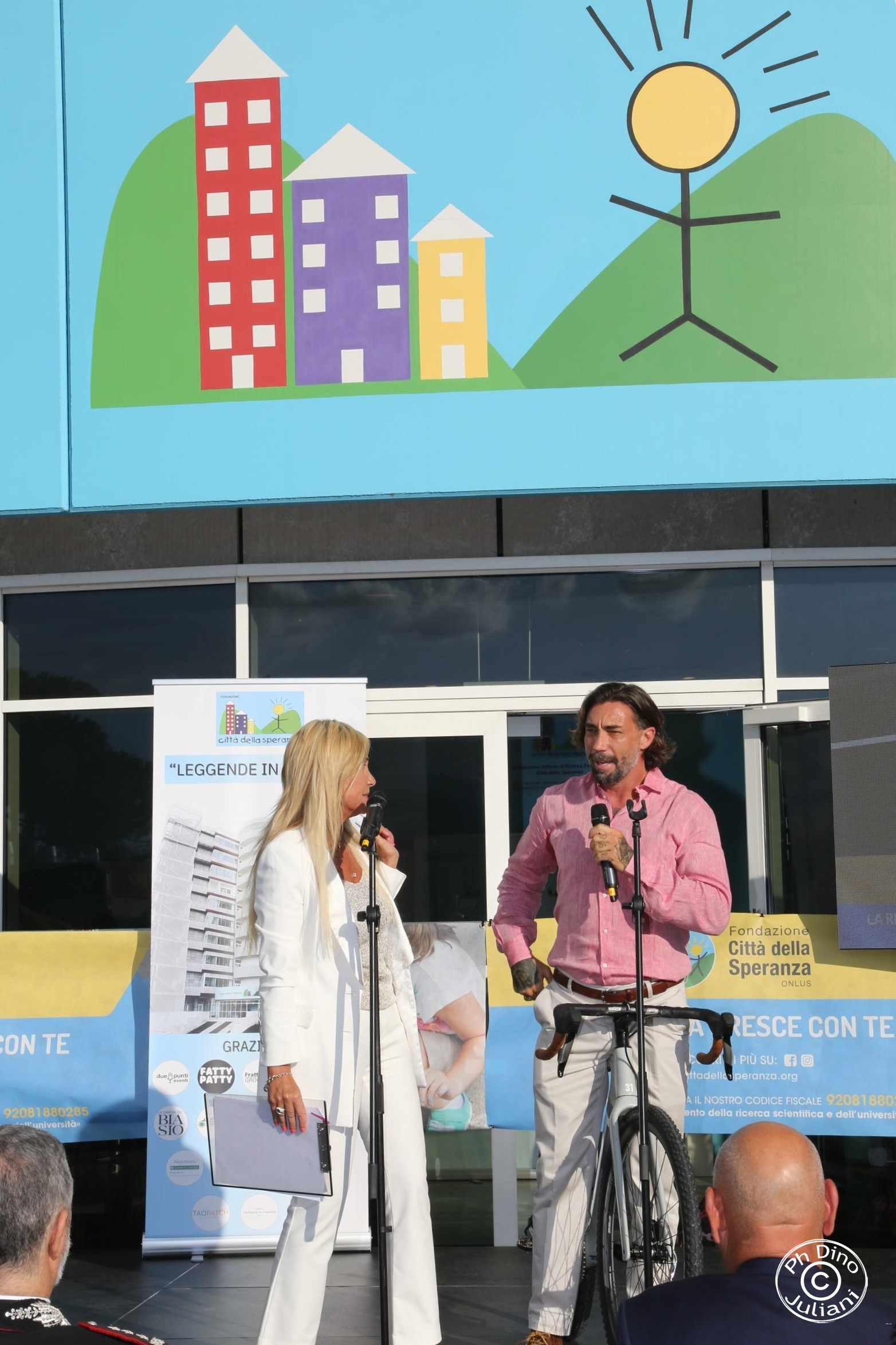 due persone sul palco davanti all'ingresso di Città della Speranza per un evento all'aperto