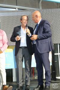 Due uomini che parlano sul microfono, uno tiene un premio a forma di stella.