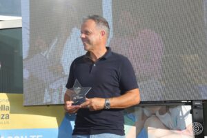 Uomo sorridente tiene un trofeo a forma di stella. Un momento di celebrazione all’insegna della passione sportiva e della solidarietà.