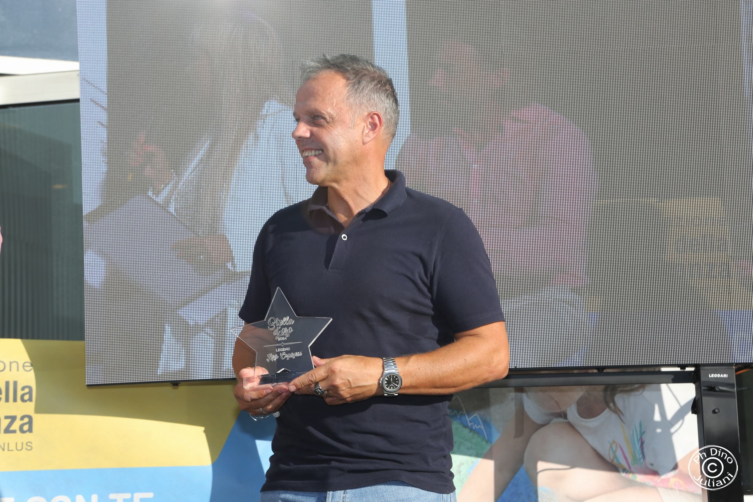 Uomo sorridente tiene un trofeo a forma di stella. Un momento di celebrazione all’insegna della passione sportiva e della solidarietà.