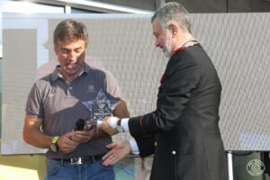 Cerimonia pubblica all’aperto con un ufficiale dei Carabinieri che da un premio a un personaggio noto in un contesto legato a sport, beneficenza o sensibilizzazione sociale.