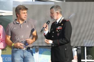 un uomo in uniforme sta parlando al microfono a un'altra persona che tiene in mano un premio