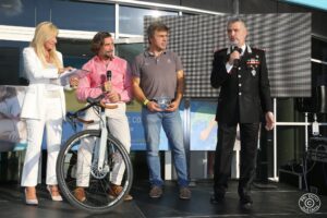 quattro persone su un palco dove uno in. uniforme sta parlando al microfono mentre gli altri ascoltano