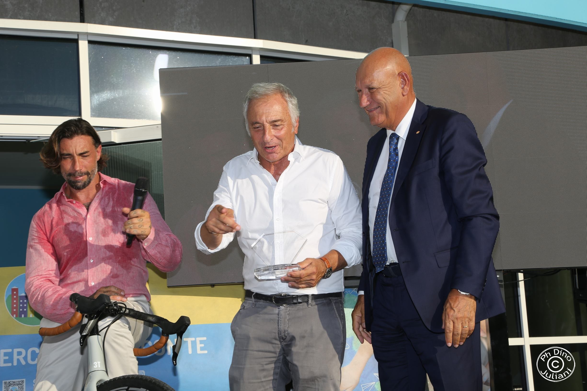 Tre persone sorridono durante una premiazione all’evento “Leggende in Torre” della Fondazione Città della Speranza.