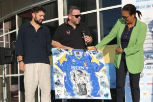re persone mostrano un quadro con una maglia storica della Juventus e l’immagine di un calciatore che solleva la Champions League, durante un evento all’aperto.