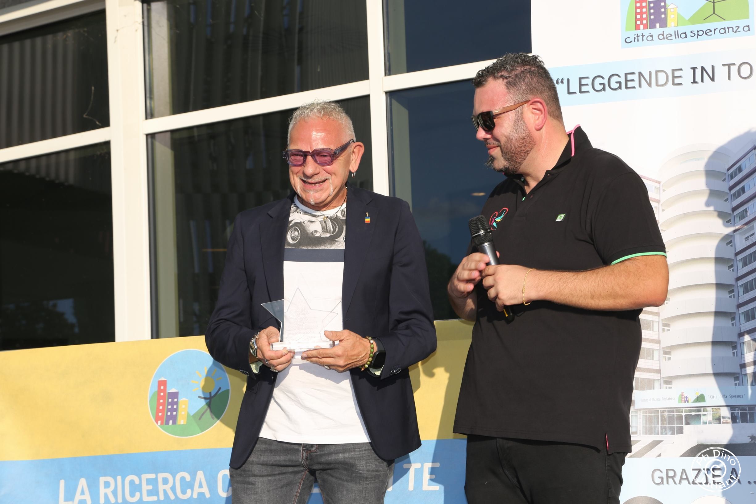 2 uomini sul palco per l'evento leggende in torre. uno tiene un premio a forma di stella in mano e uno tiene un microfono