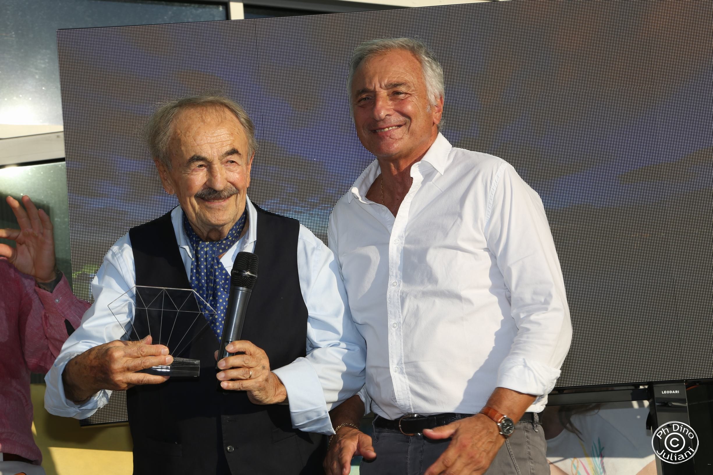 due uomini davanti all’ingresso dell’Istituto di Ricerca Pediatrica "Città della Speranza", uno tiene un premio e un microfono.