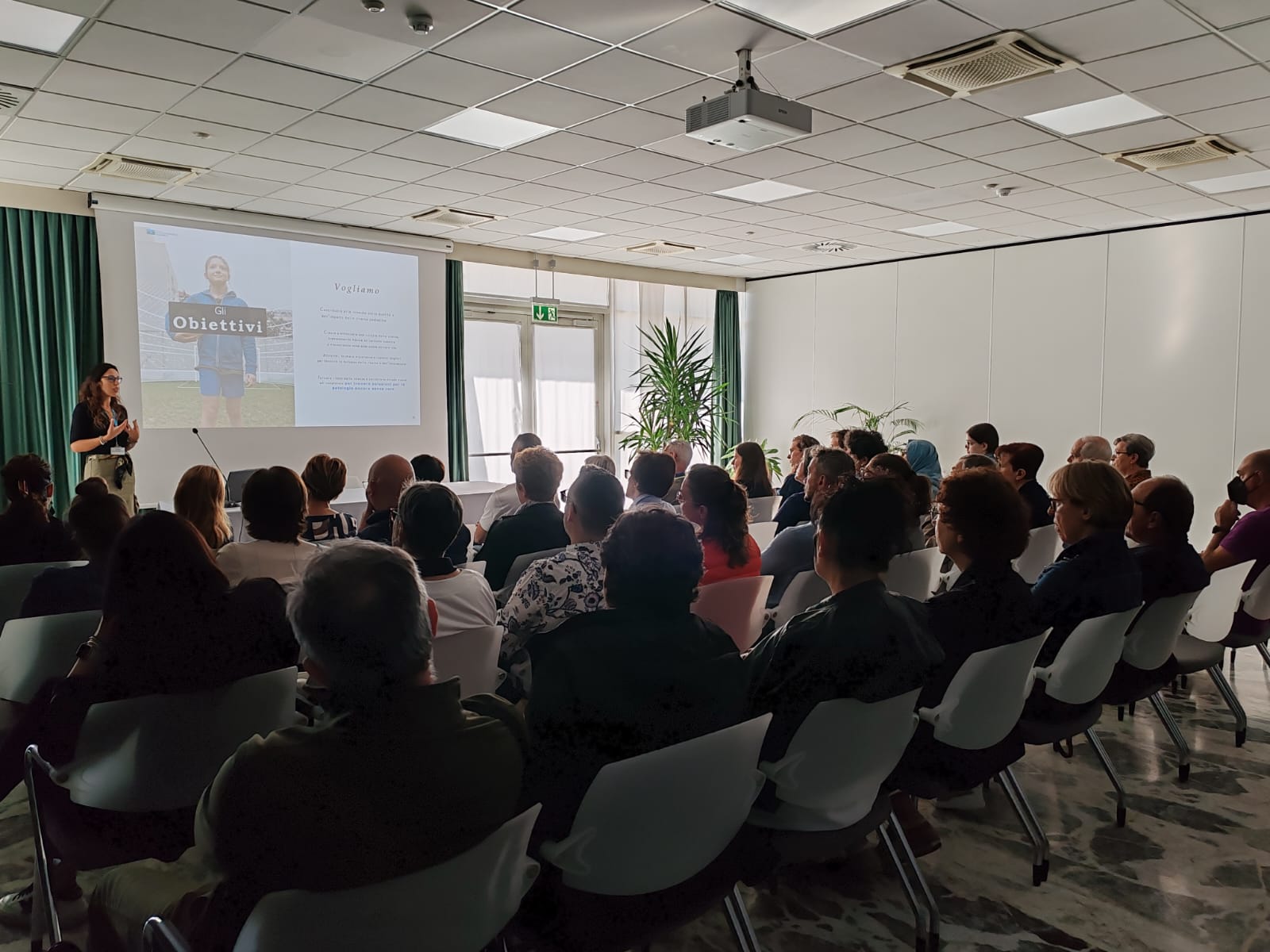 sala con gente che ascoltano il relatore che parla di obiettivi di Città della Speranza