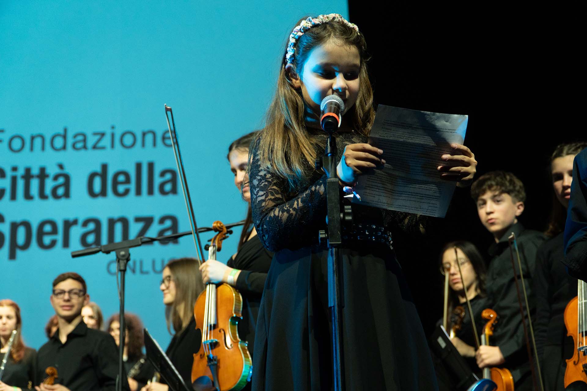 Ragazza con vestito nero che parla sul palco alla festa dell'anniversario di Città della Speranza