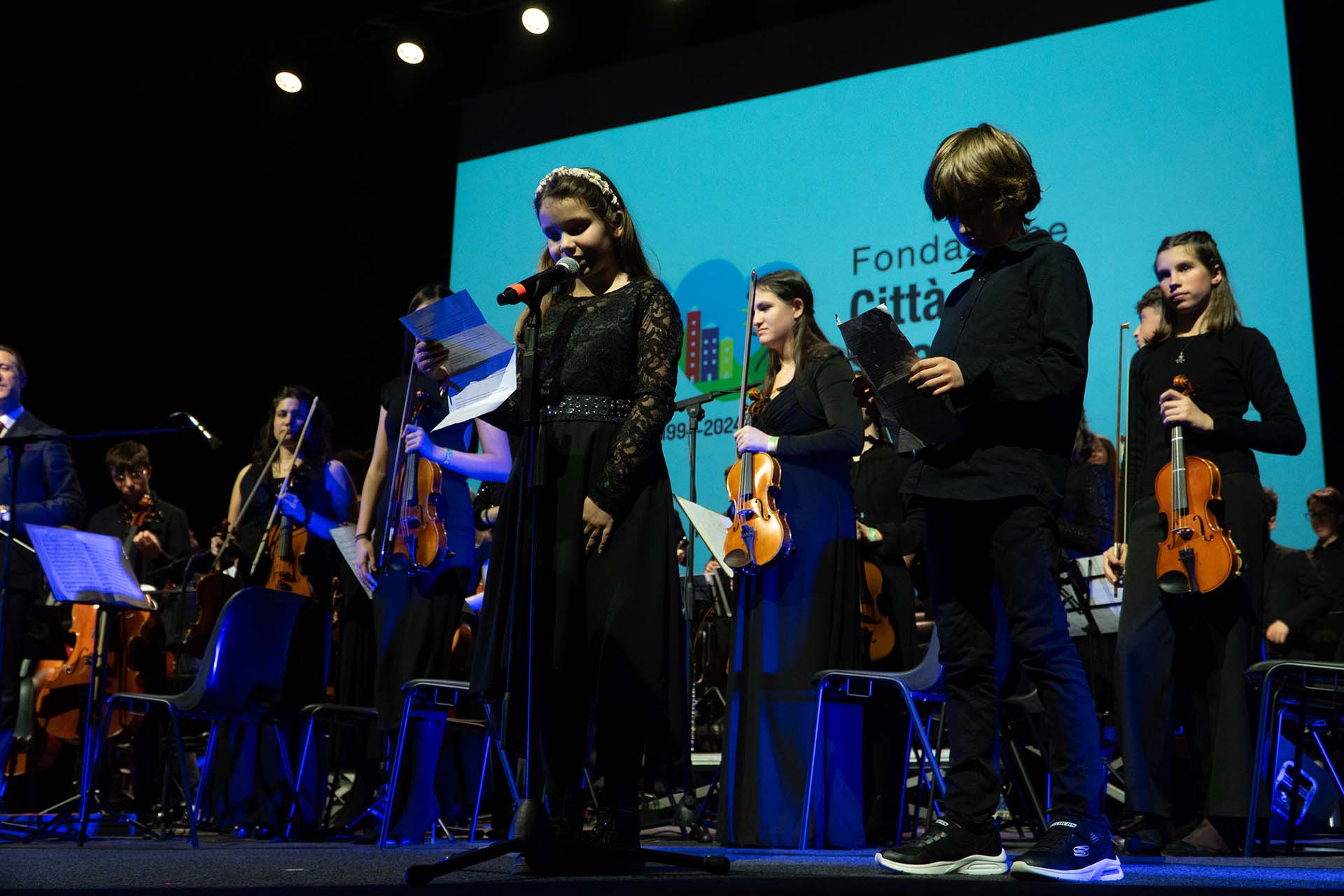 Orchestra dei Polli(ci)ni di Padova che suonano alla festa dell'anniversario trentennale di Città della Speranza con ragazza che canta