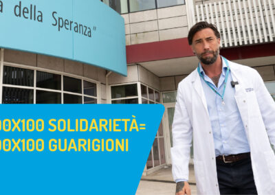 Brumotti davanti all'ingresso di Città della Speranza con la scritta 100x100 solidarietà=100x100 guarigioni